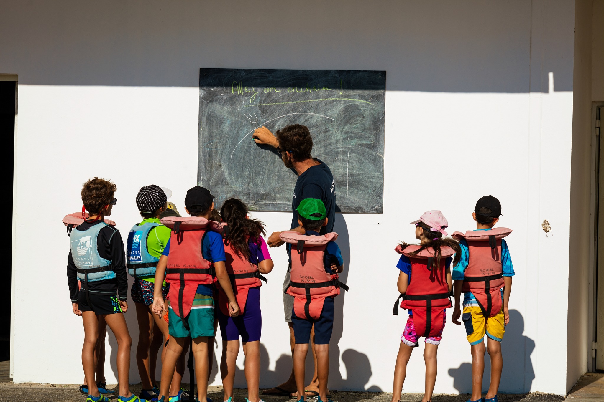 un jeune explique devant un tableau noir explique quelque chose à des enfants prêts à naviguer